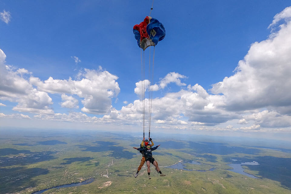 Tandem pair of skydivers under a blue, red, and white parachute. 