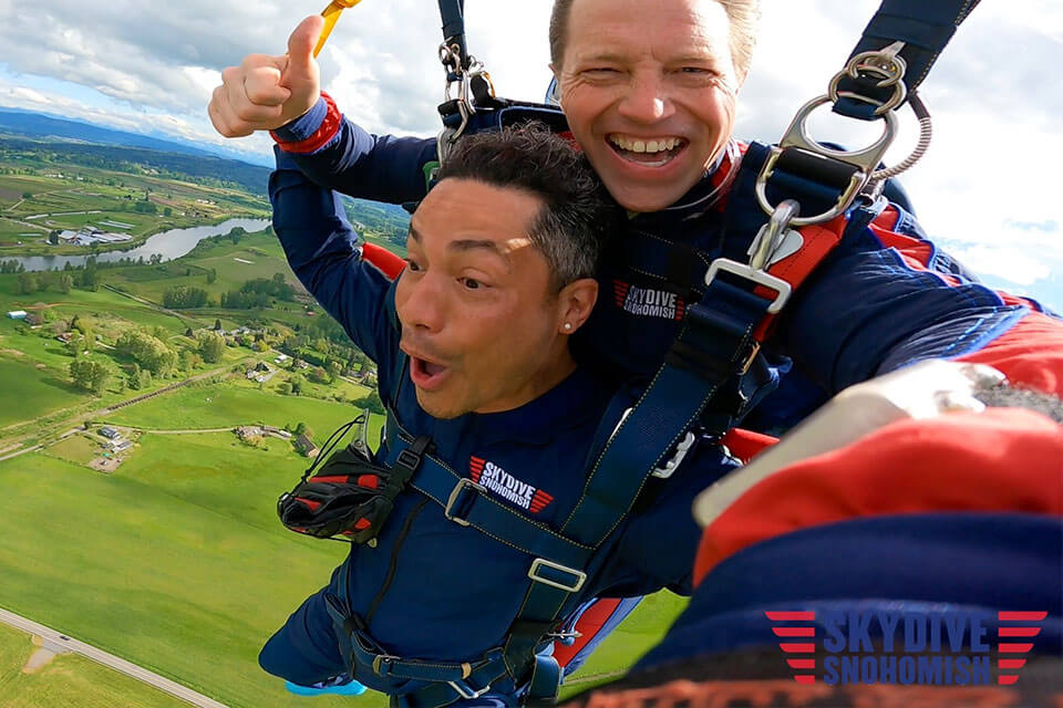 Smiling male tandem pair over the green grass and lake river at Skydive Snohomish. 