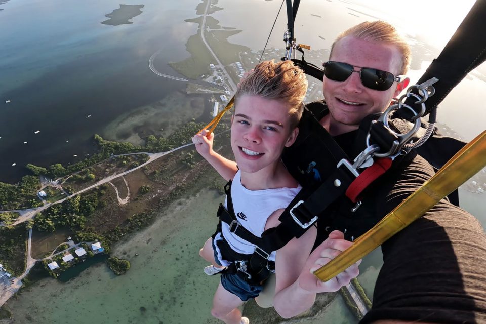 Young male wearing white nike shirt guides canopy over beautiful Florida Keys water while skydiving at Skydive Key West