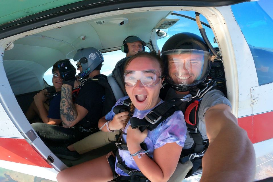 Woman in tie dye tee shirt smiles in her tandem skydiving harness on the airplane of Skydive Keywest.