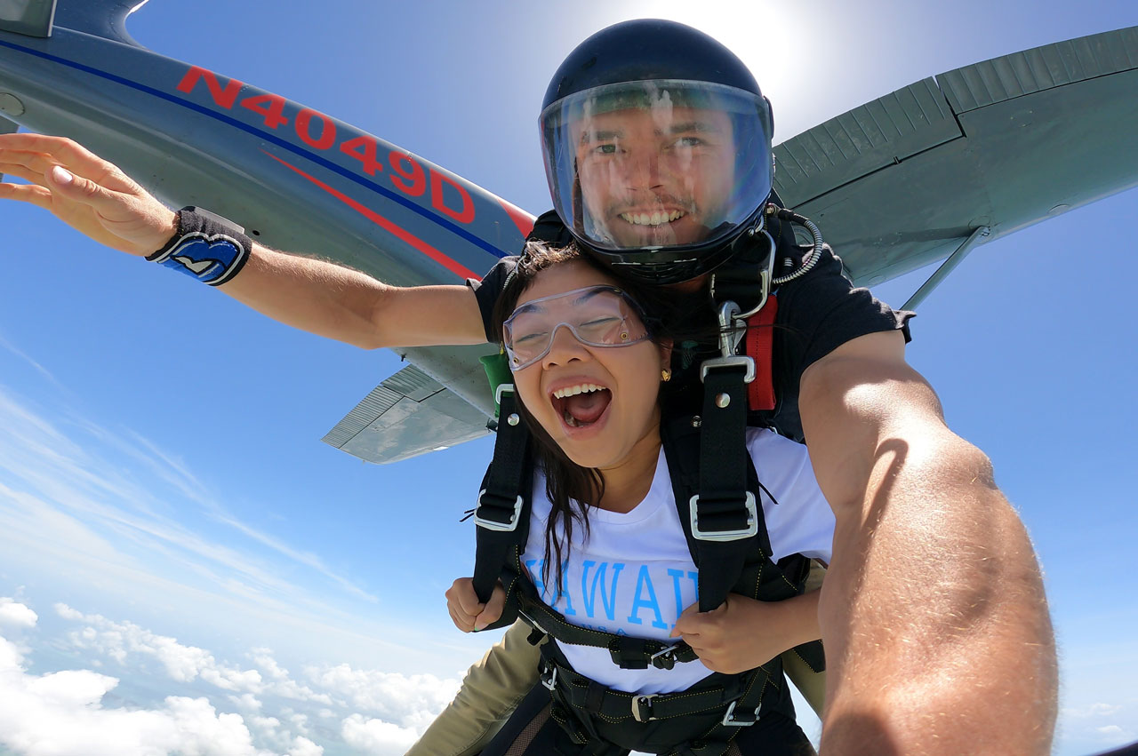 Female tandem skydiver wearing a white shirt with blue writing takes the leap out of the Skydive Key West airplane into free fall