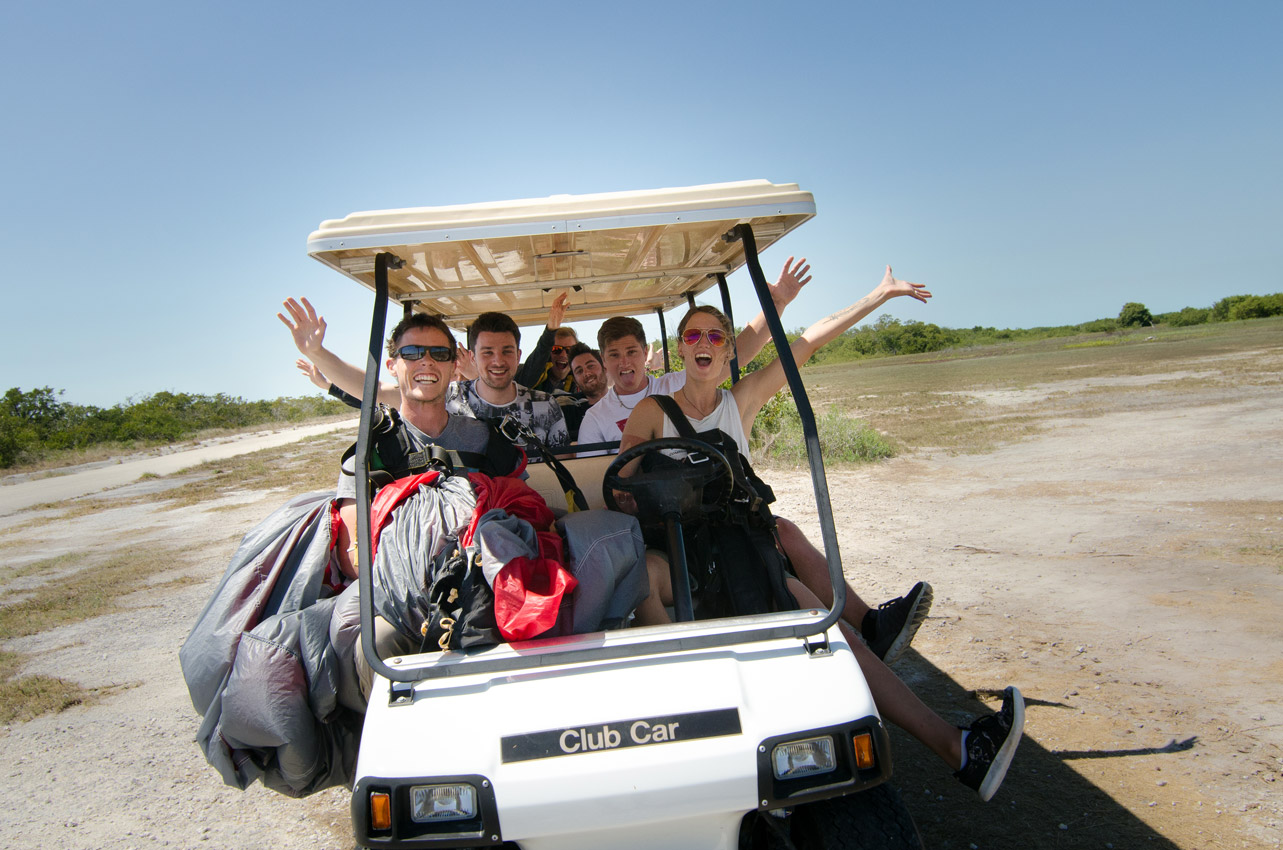 Young people smile with arms stretched out while in a golf cart after enjoying a skydive at Skydive Key West
