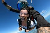 Female tandem skydiver with white shirt smiles with her mouth wide open.