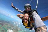young female with yellow shirt points and smiles during her jump at skydive key west