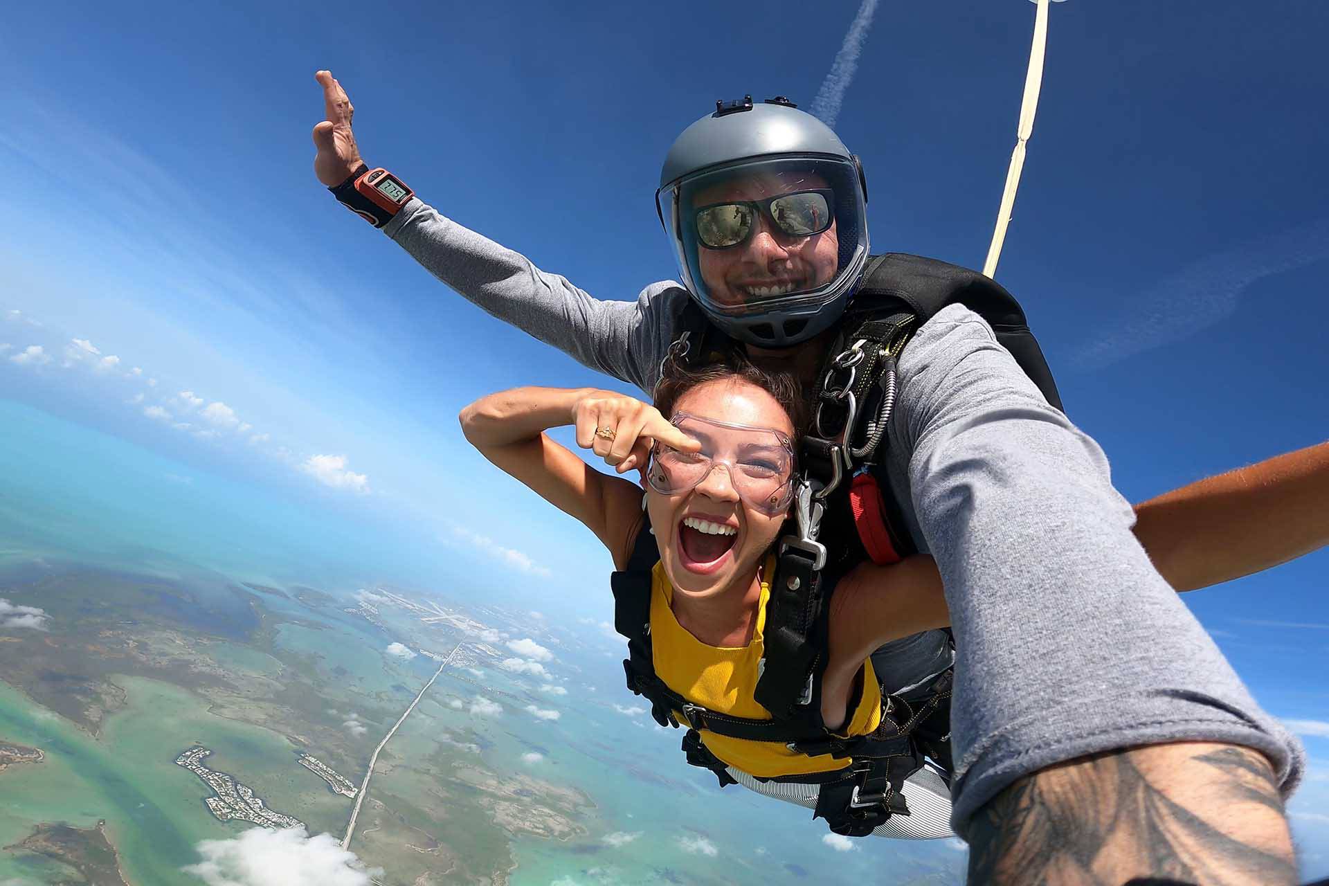 Female tandem skydiving student in a yellow t-shirt smiling for a photo while jumping over the Florida Keys