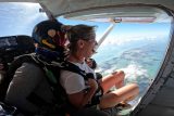 Female wearing white shirt and shorts gets ready to leap from Skydive Key West airplane with tandem instructor