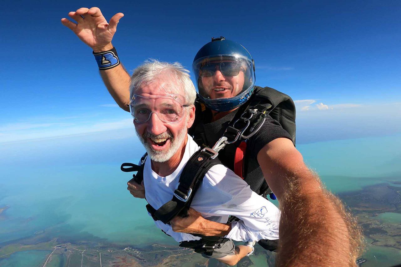 older gentlemen wearing a white long sleeve shirt smiles during his Florida Keys Skydiving experience