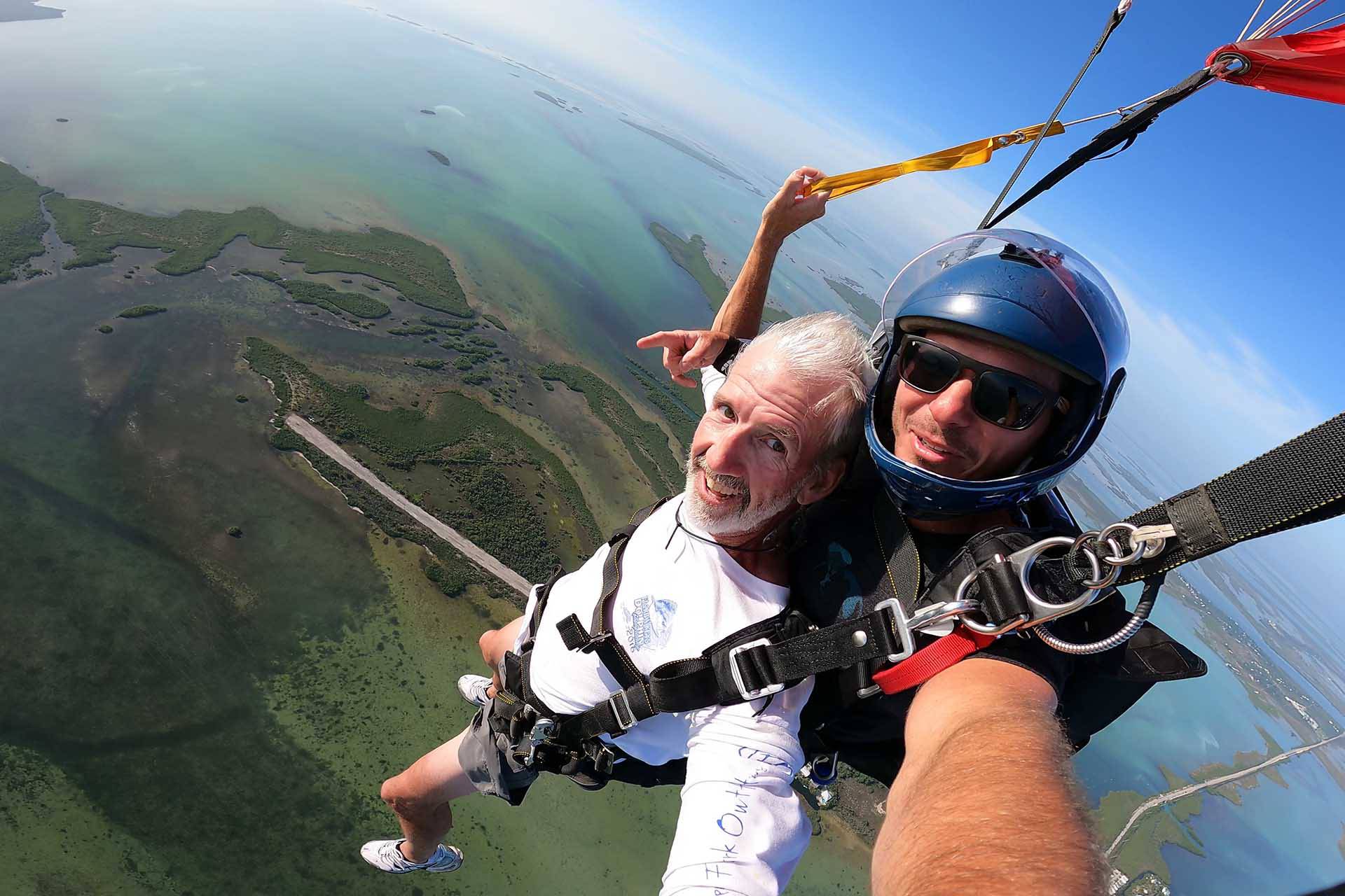 Older gentlemen wearing white shirt smiles while Skydiving South Florida