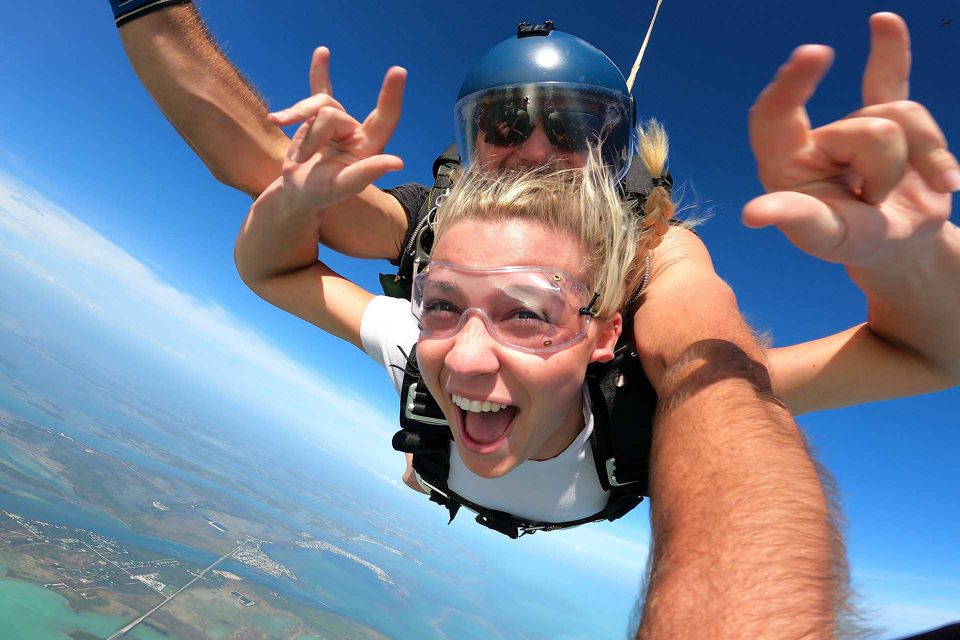 Blond haired female wearing white shirts smiles during an amazing skydive at Skydive Key West