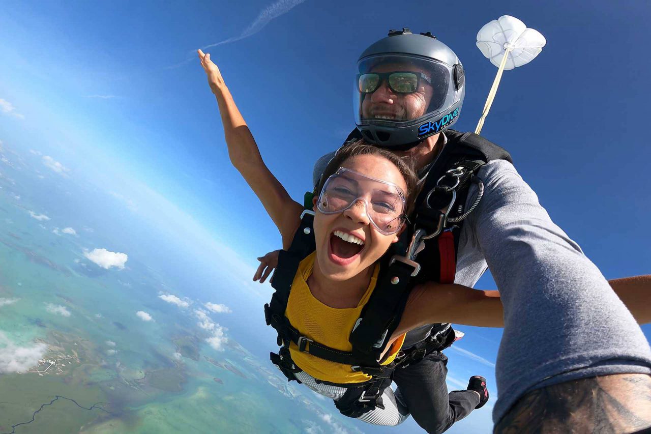 Young female wearing yellow shirt smile and outstretches her arms during her jump at Skydive Key West