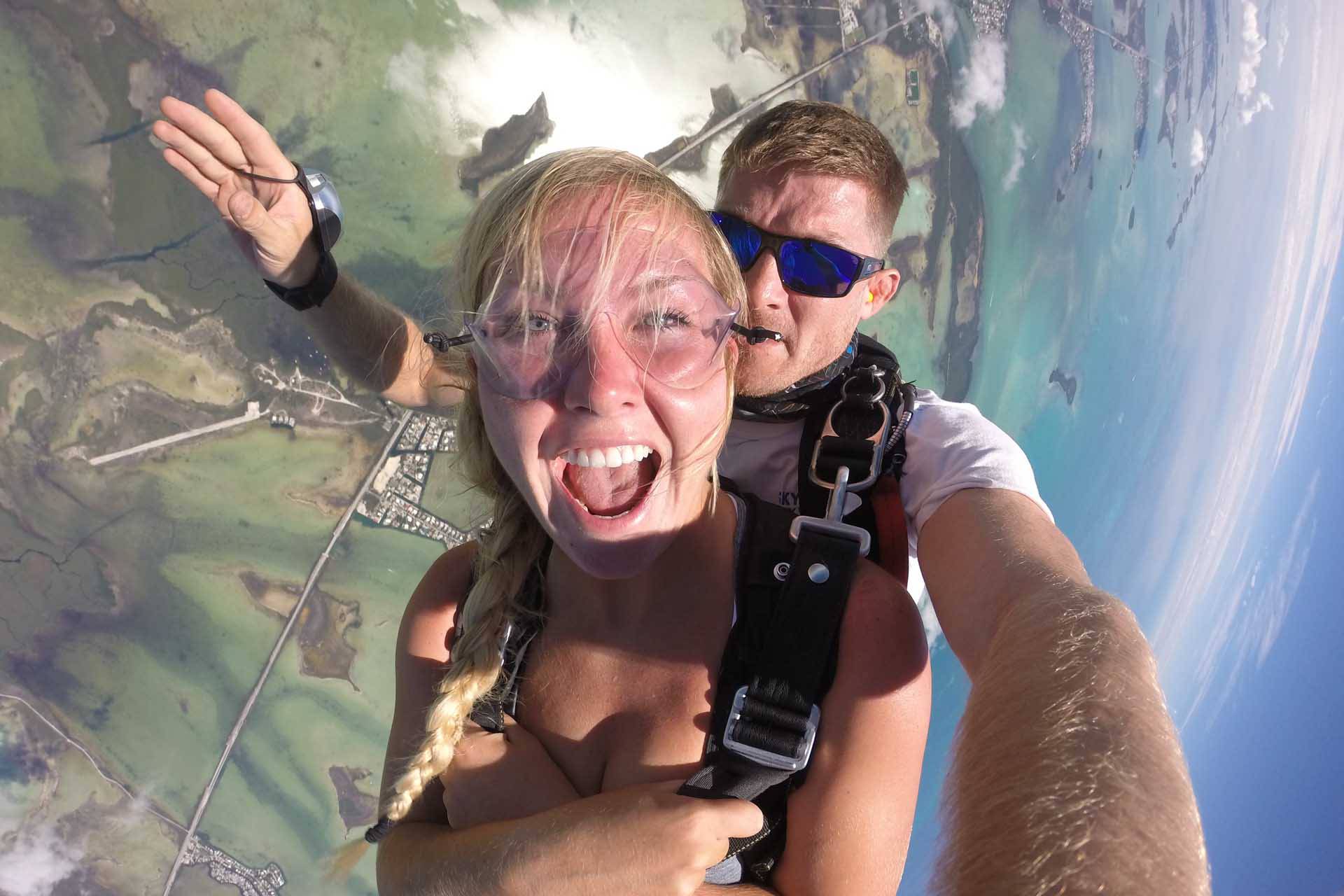 Young female with her hair in a braid folds arms against her chest while in free fall with Skydive Key West tandem instructor