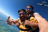Young man with dark hair gleaming with joy during freefall as Skydive Key West plane flies above him