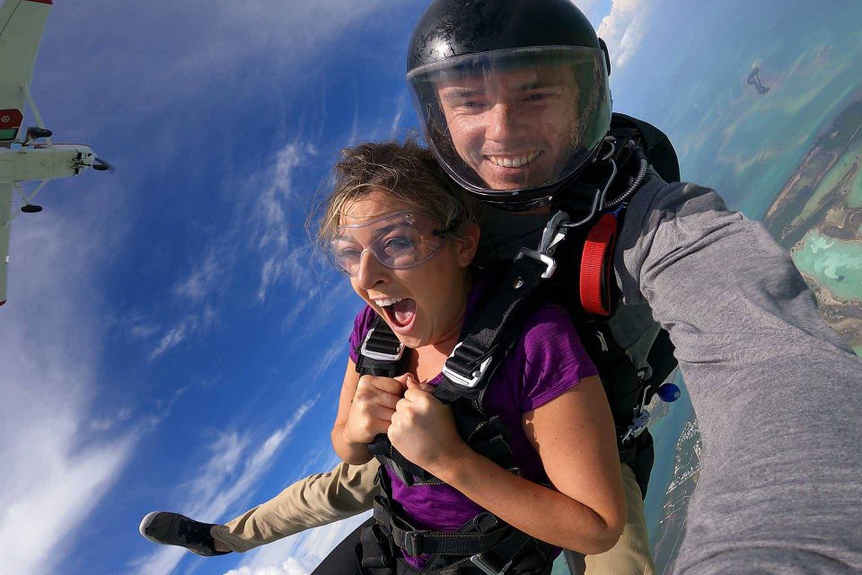 Woman wearing purple shirt skydives with bright blue clouds above her with Skydive Key West tandem instructor