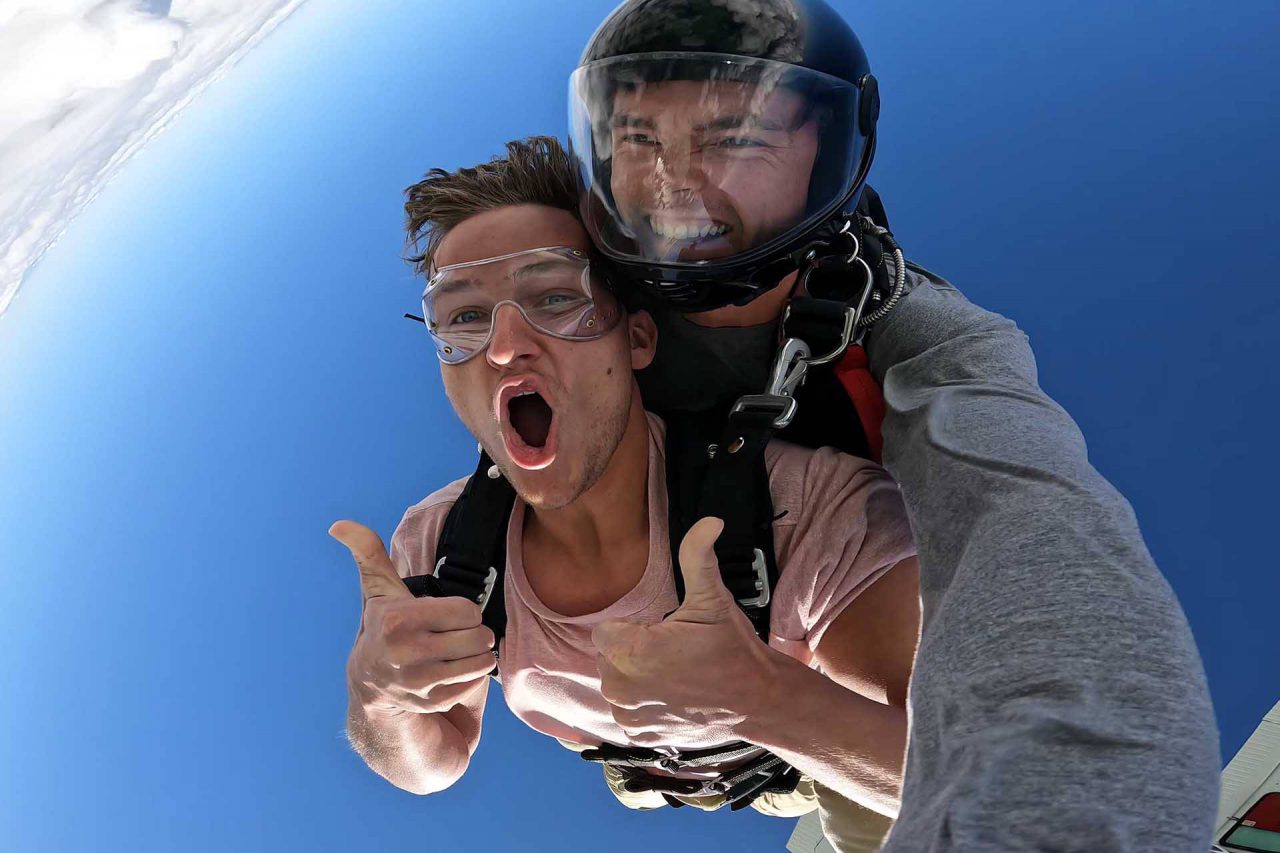 Young man wearing a pink shirt gives two thumbs up during his jump at skydive key west