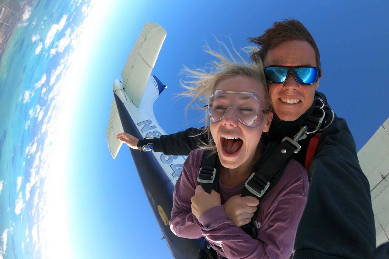 Young female wearing purple shirt takes the leap from a Skydive Key West airplane into free fall