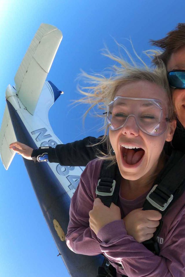 Young female wearing purple shirt takes the leap from a Skydive Key West airplane into free fall