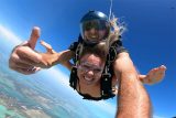 Skydive Key West Tandem instructor wearing blue hemet gives a thumbs up while in free fall with tandem student.