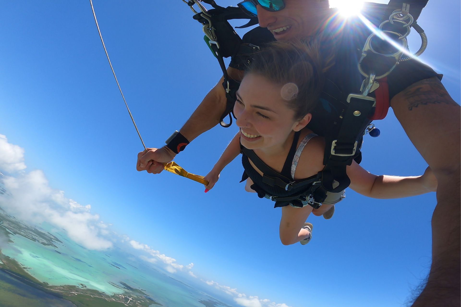 Female tandem student in a tank tops helps the instructor steer by pulling the yellow toggle under canopy.