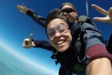 Smiling tandem skydiving student holds up two fingers on each hand during freefall to show peace signs.