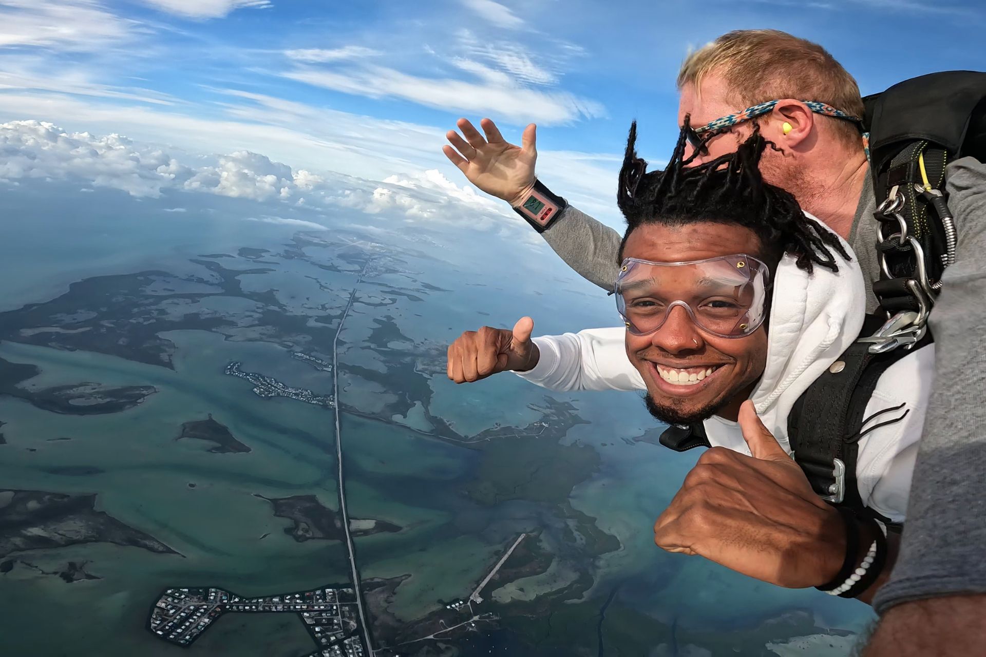 Male tandem skydiver in a white hoodie gives thumbs up. 