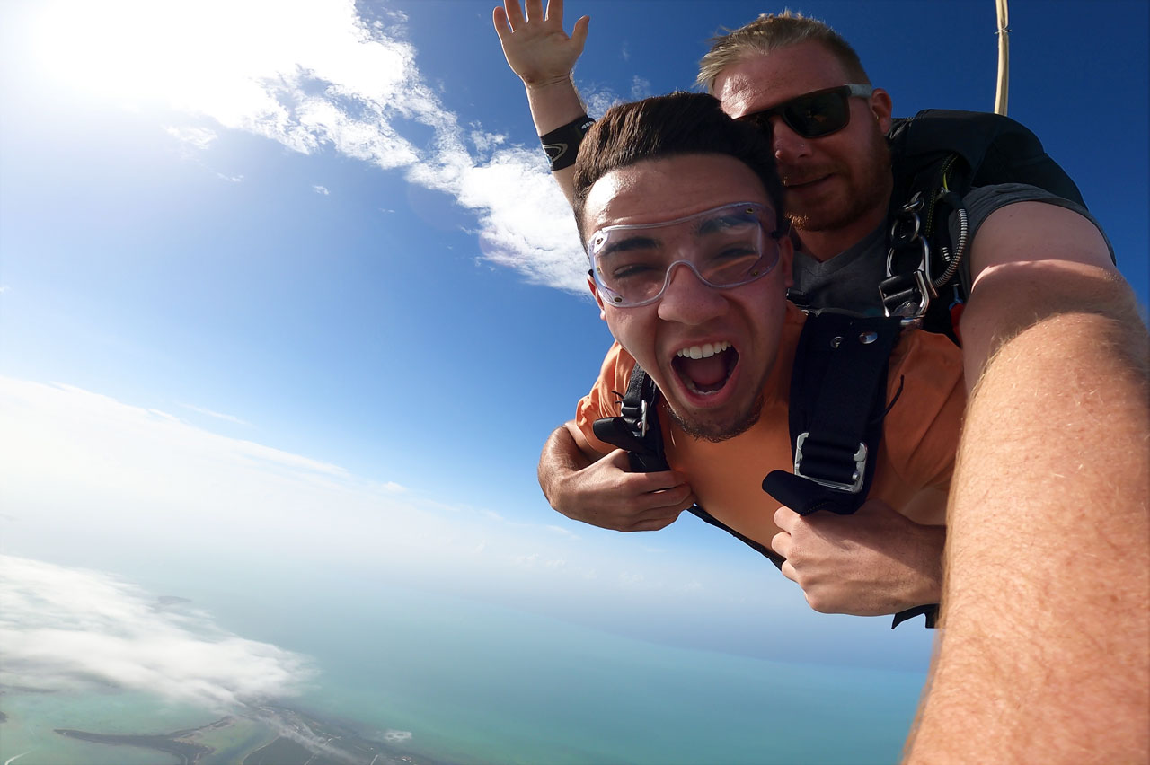 Young male wearing an orange shirt enjoys tandem skydiving with Skydive Key West instructor