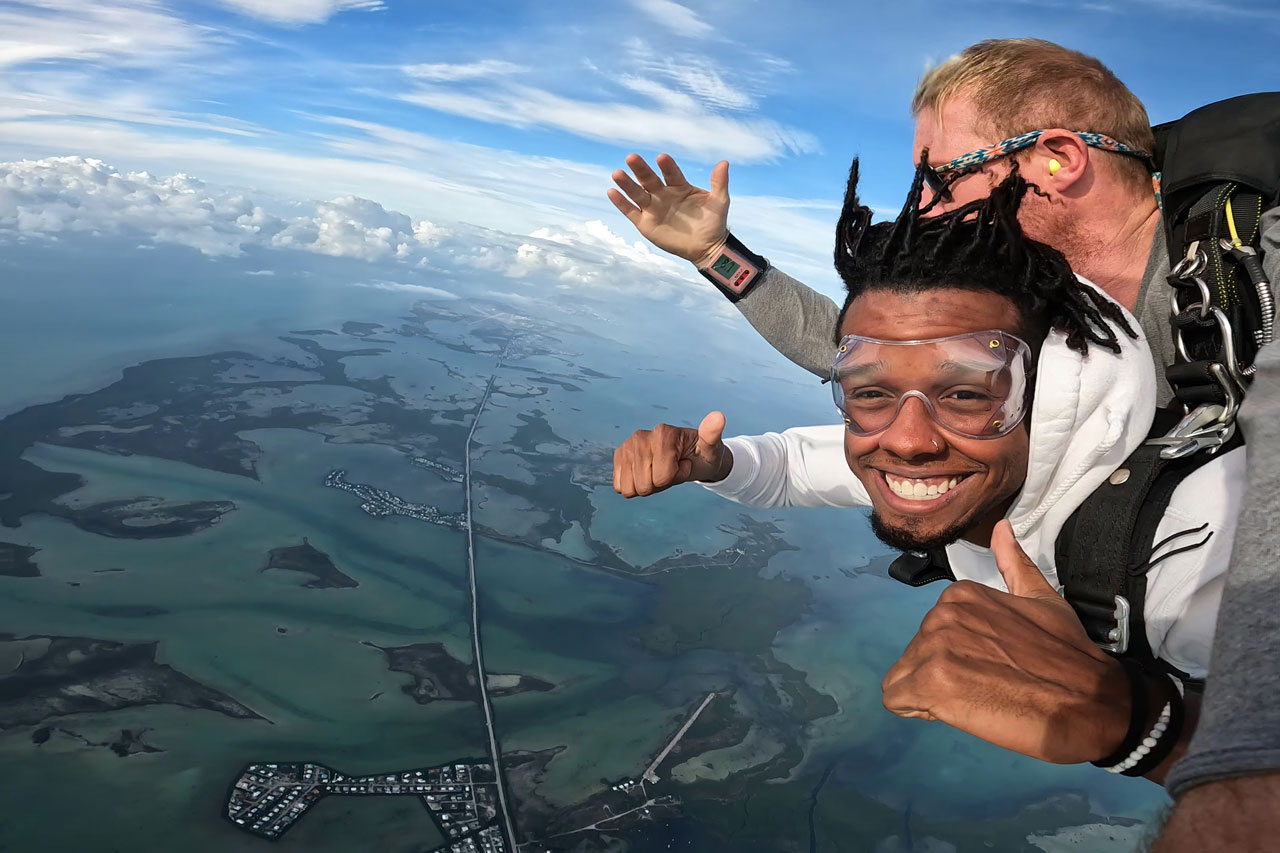 Young male gives thumbs up and smiles while tandem skydiving in south florida