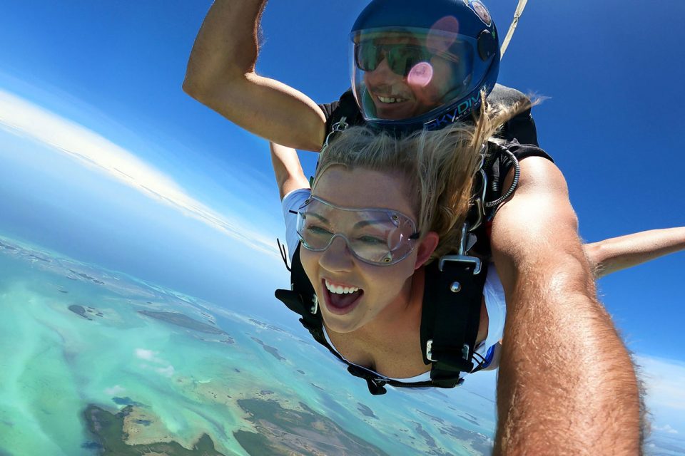 young female with blond hair out stretches her arms while in freefall over Florida Keys